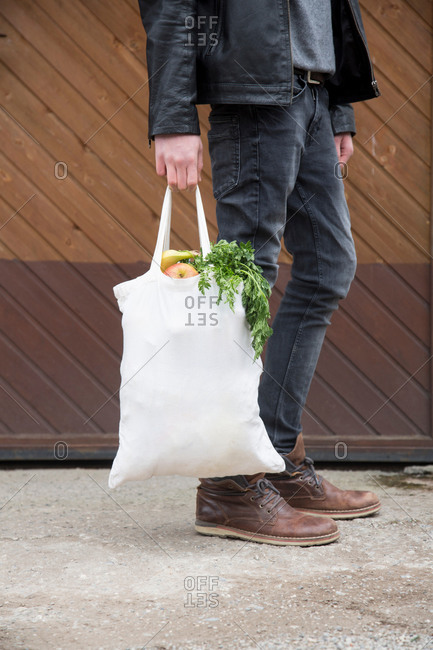 Teenage boy carrying reusable shopping bags full of fresh fruit and veg
