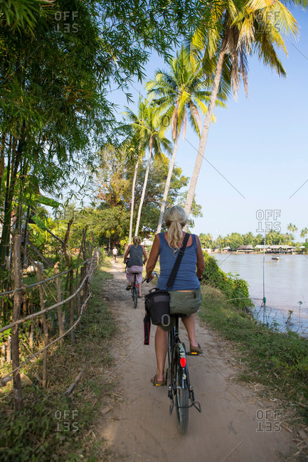 Rear view of two female tourists cycling on Mekong riverbank, Don Det, Laos