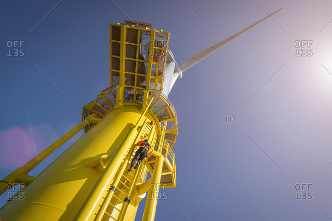 Low angle view of engineers climbing turbine from ship at offshore windfarm