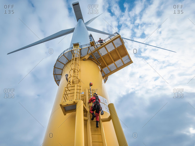 Low angle view of engineers climbing wind turbine from ship at offshore windfarm