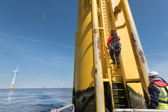 Engineers climbing wind turbine ladder from boat at offshore windfarm