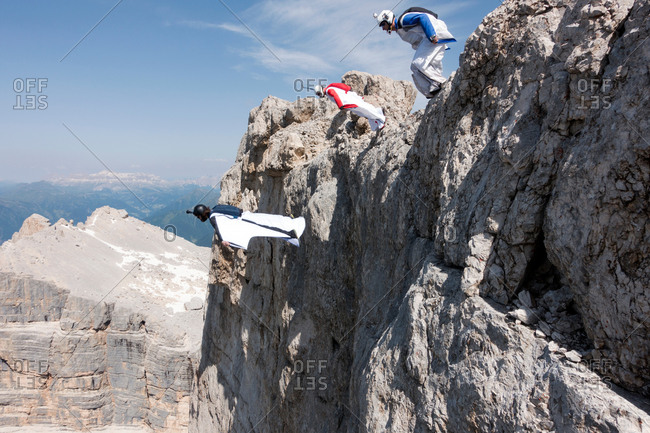 Three male BASE jumpers exiting from mountain top, Dolomites, Italy
