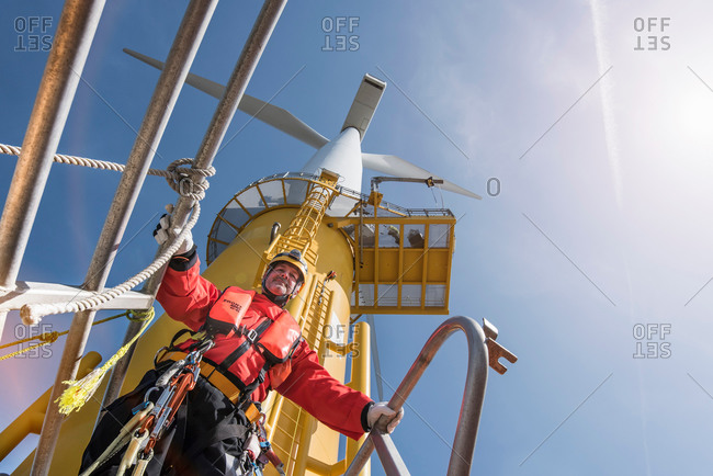 Engineer preparing to climb wind turbine at offshore windfarm, low angle view