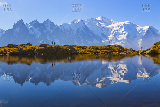 Two hikers in front of Mont Blanc which is reflected in a scenic mountain lake near Chamonix, France.