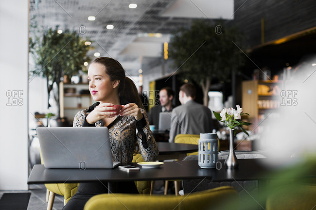 Confident businesswoman with laptop drinking coffee at table in restaurant