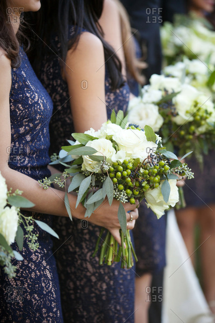 Bridesmaids in navy lace dresses holding white floral bouquet