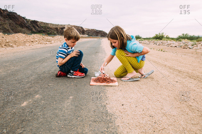 Brother and sister working on a baking soda volcano experiment on the side of the road