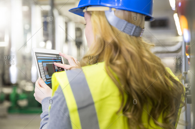 Woman wearing reflective vest controlling industrial plant with digital tablet