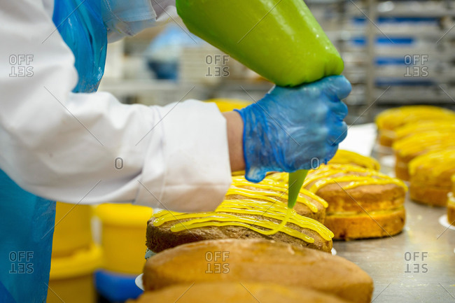 Female worker piping lemon icing onto cakes in cake factory, close up