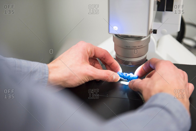Male worker looking at components through microscope at tool manufacturing plant, focus on hands
