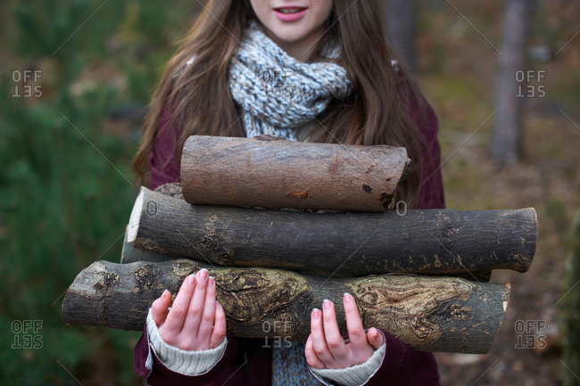 Young woman collecting logs for campfire in forest