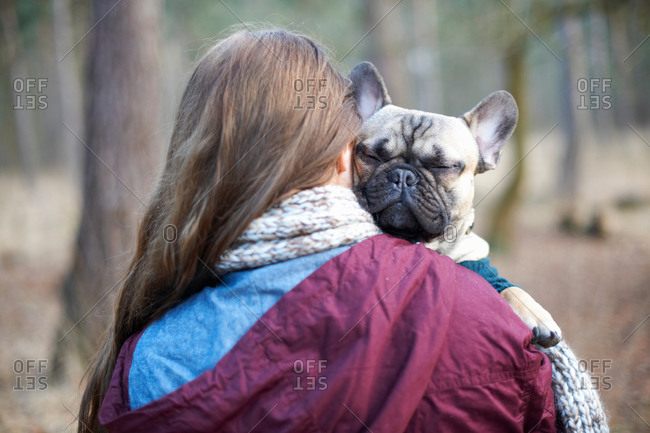 Portrait of cute dog being carried through forest by young woman