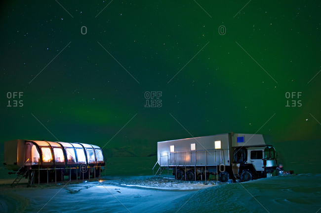 Aurora borealis and parked mobile hotel trucks at night, South East Iceland