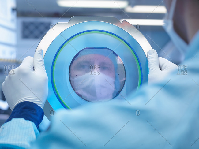 Electronics worker reflected in silicon wafer in clean room laboratory