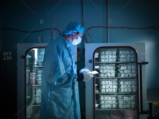 Worker using digital tablet to check archived electronic components in nitrogen atmosphere in clean room laboratory