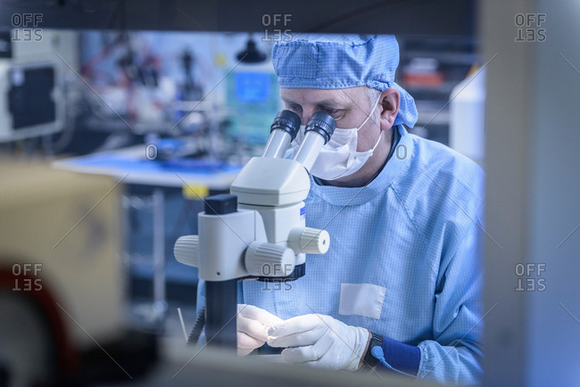 Electronics worker checking component with microscope in clean room