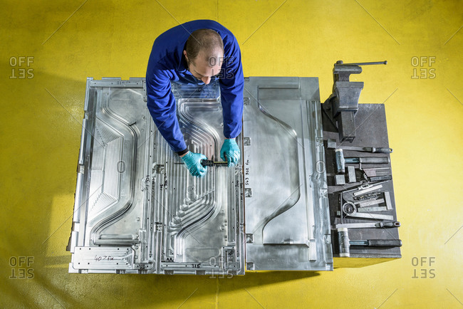 Overhead view of worker finishing metal mould in plastics factory