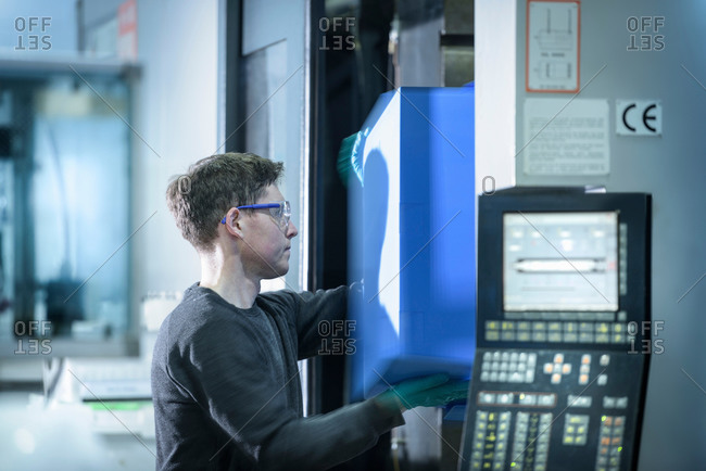 Worker removing plastic part from injection moulding machine in plastics factory