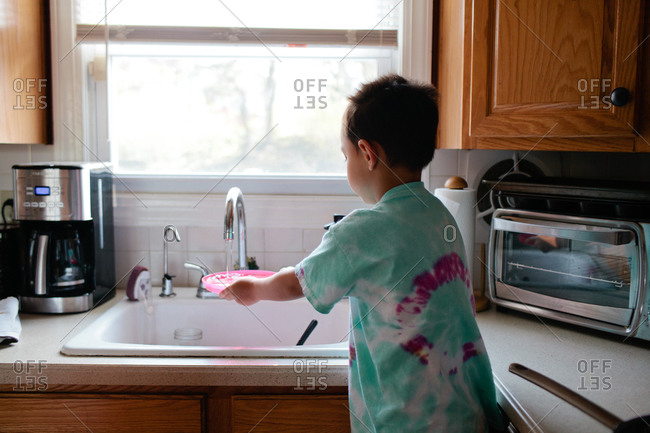 Young boy washing a plate in the sink