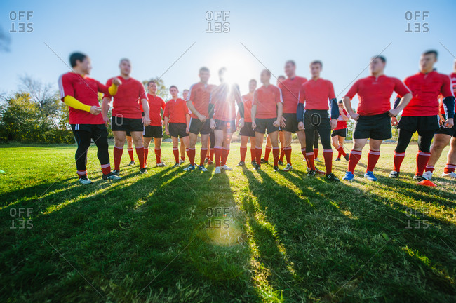 Rugby Union players standing in line on football field, preparing for the game with sun behind them and big shadows on the green field with focus on legs