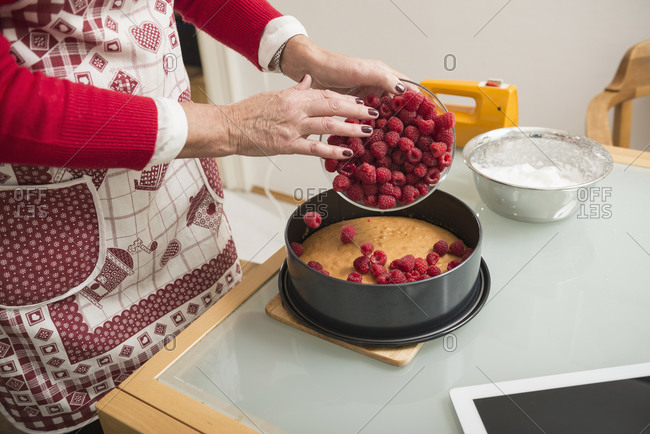 Senior woman spreading raspberries on cake base in spring form pan, Munich, Bavaria, Germany