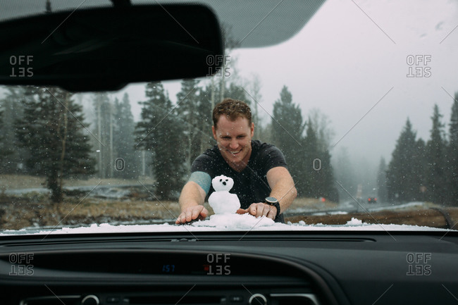 Man building snowman on car