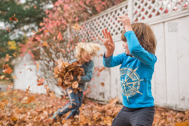 Two boys playing outside in a yard full of autumn leaves