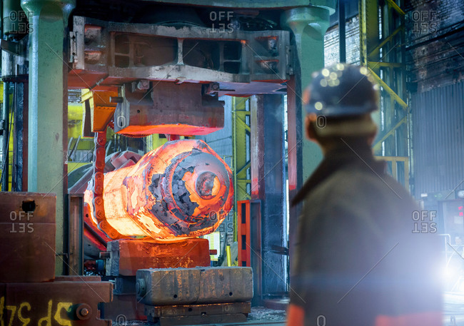 Steelworker inspects hot steel in forging press
