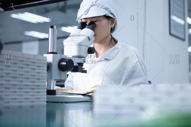 Worker at a microscope in factory that specializes in creating functional circuits on flexible surfaces
