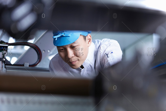 Worker leaning over a machine in a factory that specializes in creating functional circuits on flexible surfaces