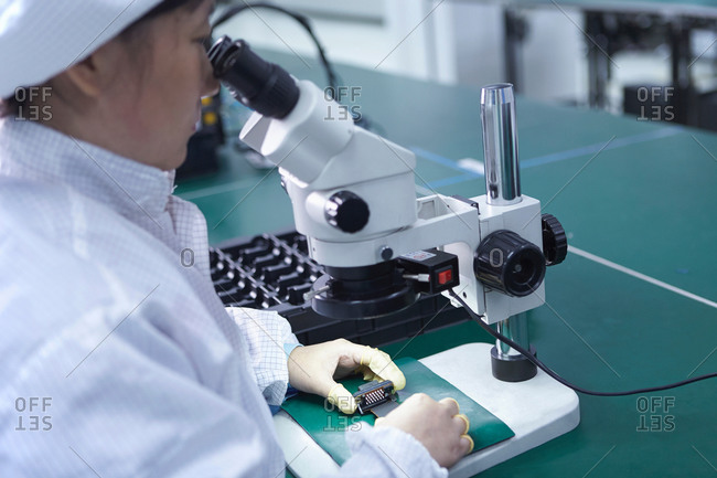 Worker looking at circuit under a microscope in factory that specializes in creating functional circuits on flexible surfaces