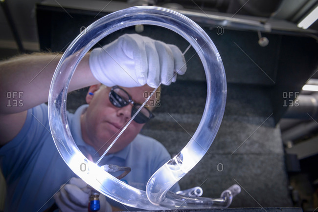 Industrial glass blower welding a curved glass tubes