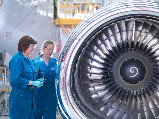 Female engineers working on engine in aircraft maintenance factory