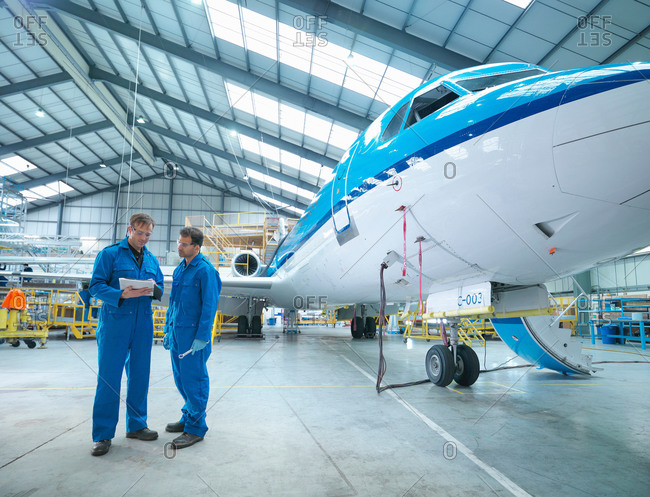 Engineers in discussion by aircraft in aircraft maintenance factory