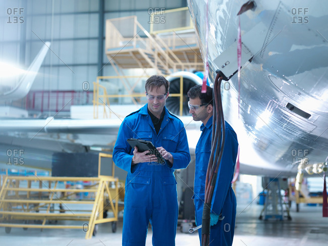 Engineers using digital tablet and in discussion in aircraft maintenance factory
