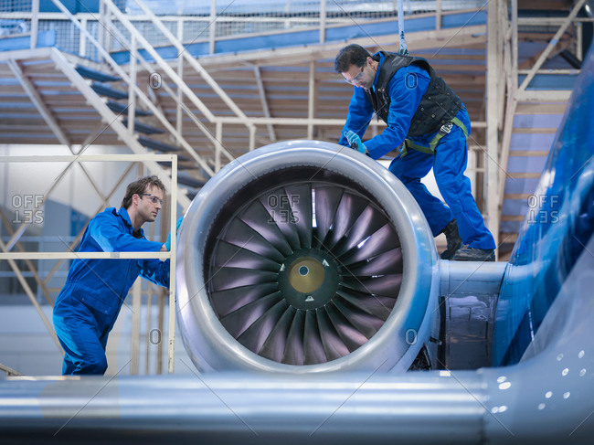 Engineers working on airplane engine in aircraft maintenance factory