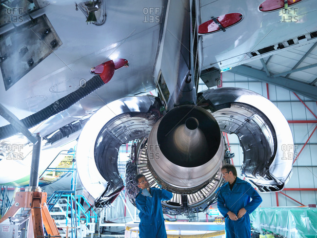 Two engineers working on jet engine in aircraft maintenance factory