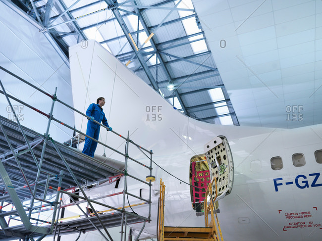 Engineer on scaffolding by aircraft in aircraft maintenance factory, low angle view
