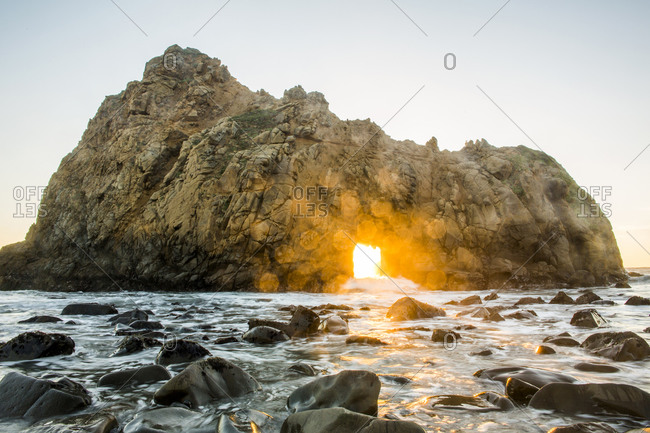 Sun shining through rock formation to ocean waves, Big Sur, California, United States