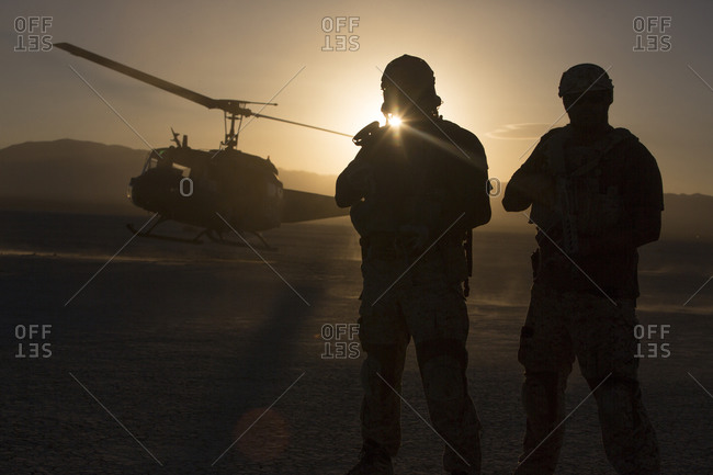Silhouette of soldiers watching helicopter in desert landscape