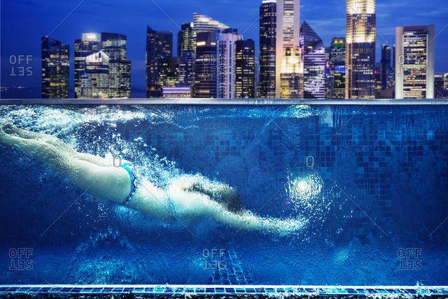 Caucasian woman swimming in urban rooftop pool in Singapore cityscape