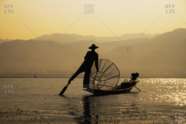 Asian fisherman rowing canoe on rural lake