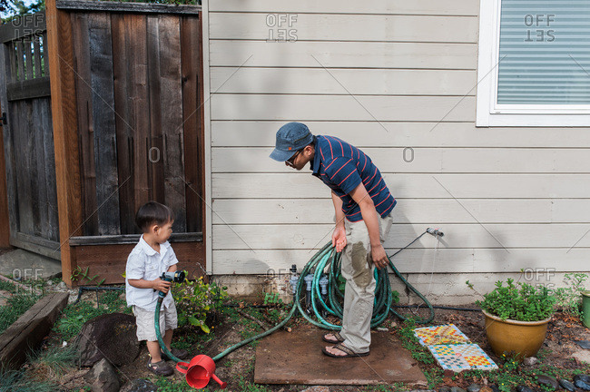 Child hold garden hose with father with wet pants