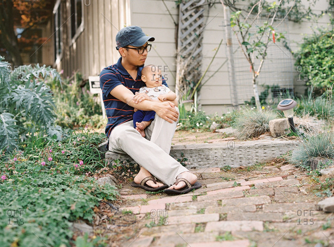 Young father in glasses and baseball hat sitting on step with his son