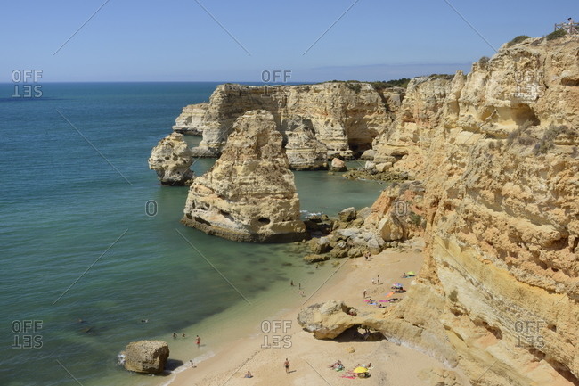 Overview of tourists on beach, sandstone cliffs and sea stacks at Praia da Marinha, Portugal