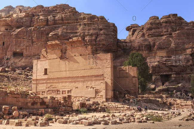 Local men on donkeys pass Qasr al-Bint temple, City of Petra ruins, Petra, Jordan, Middle East
