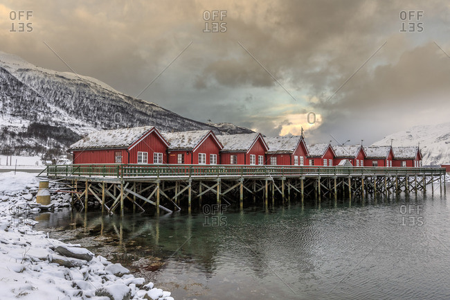 Typical red wooden huts of fishermen in the snowy and icy landscape of Lyngen Alps Tromso Lapland Norway Europe