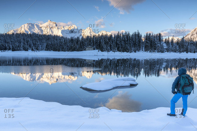 Hiker admires the snowy peaks and woods reflected in Lake Pal�_ at dawn Malenco Valley Valtellina Lombardy Italy Europe