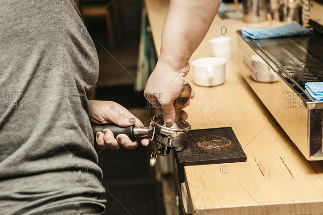 Barista packing coffee into espresso filter at cafe