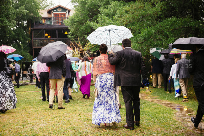 Group of people carrying umbrellas walking toward a house in the rain